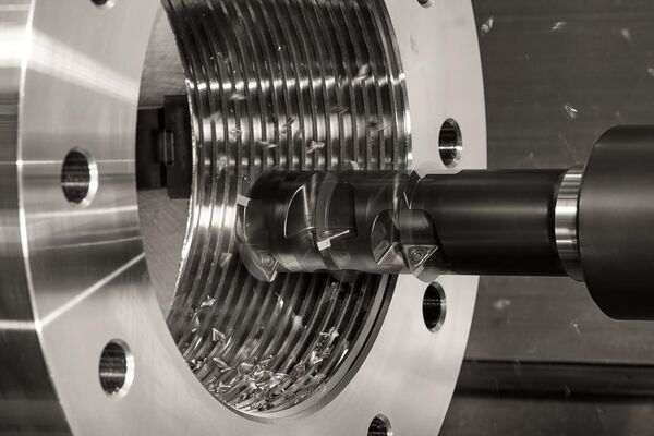 Nahaufnahme einer CNC-Maschine bei der Arbeit, mit sichtbaren Metallspaenen und einem bearbeitenden Werkstueck mit Gewinde.