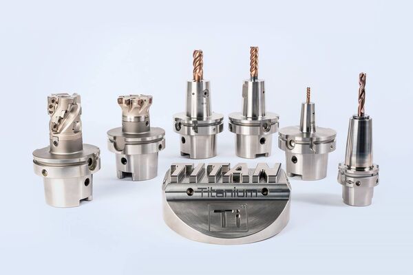 Eine Sammlung von präzisionsgefertigten Metallwerkzeugen und -komponenten für die maschinelle Bearbeitung auf einem weißen Hintergrund. Im Vordergrund liegt eine größere runde metallene Vorrichtung mit eingraviertem Wort "Titanium".