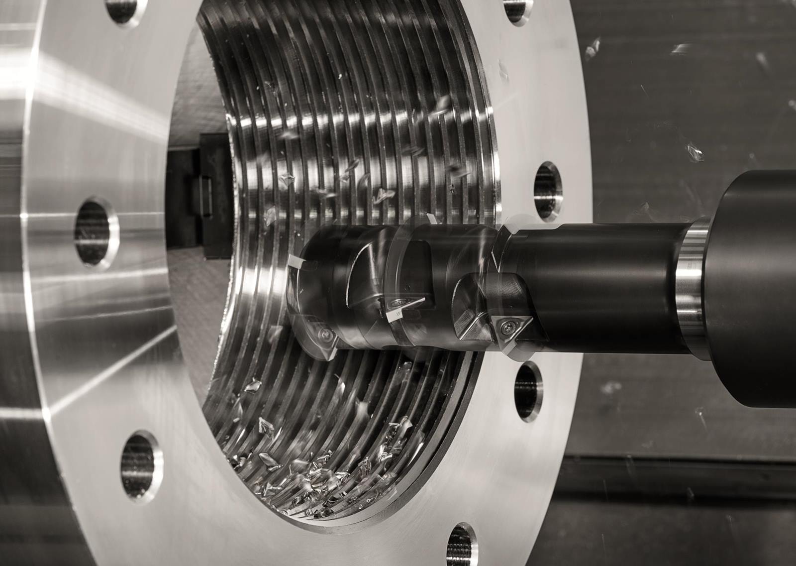 Nahaufnahme einer CNC-Maschine bei der Arbeit, mit sichtbaren Metallspaenen und einem bearbeitenden Werkstueck mit Gewinde.